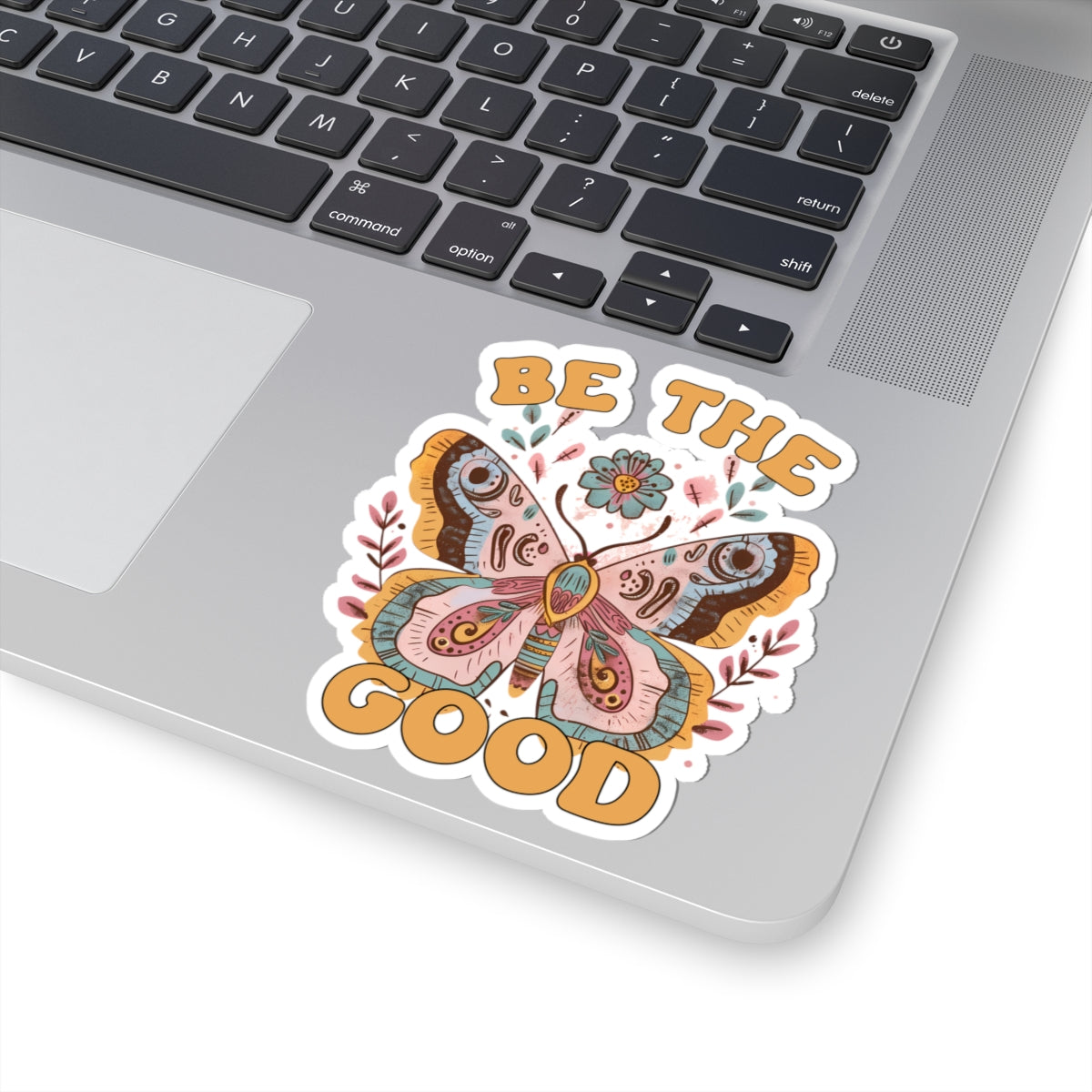 Butterfly 'Be the Good' sticker on a laptop with coffee and desk decor